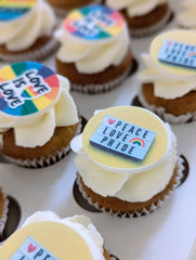 Cupcakes with 'Peace Love Pride' and rainbow-themed decorations on a white tray.