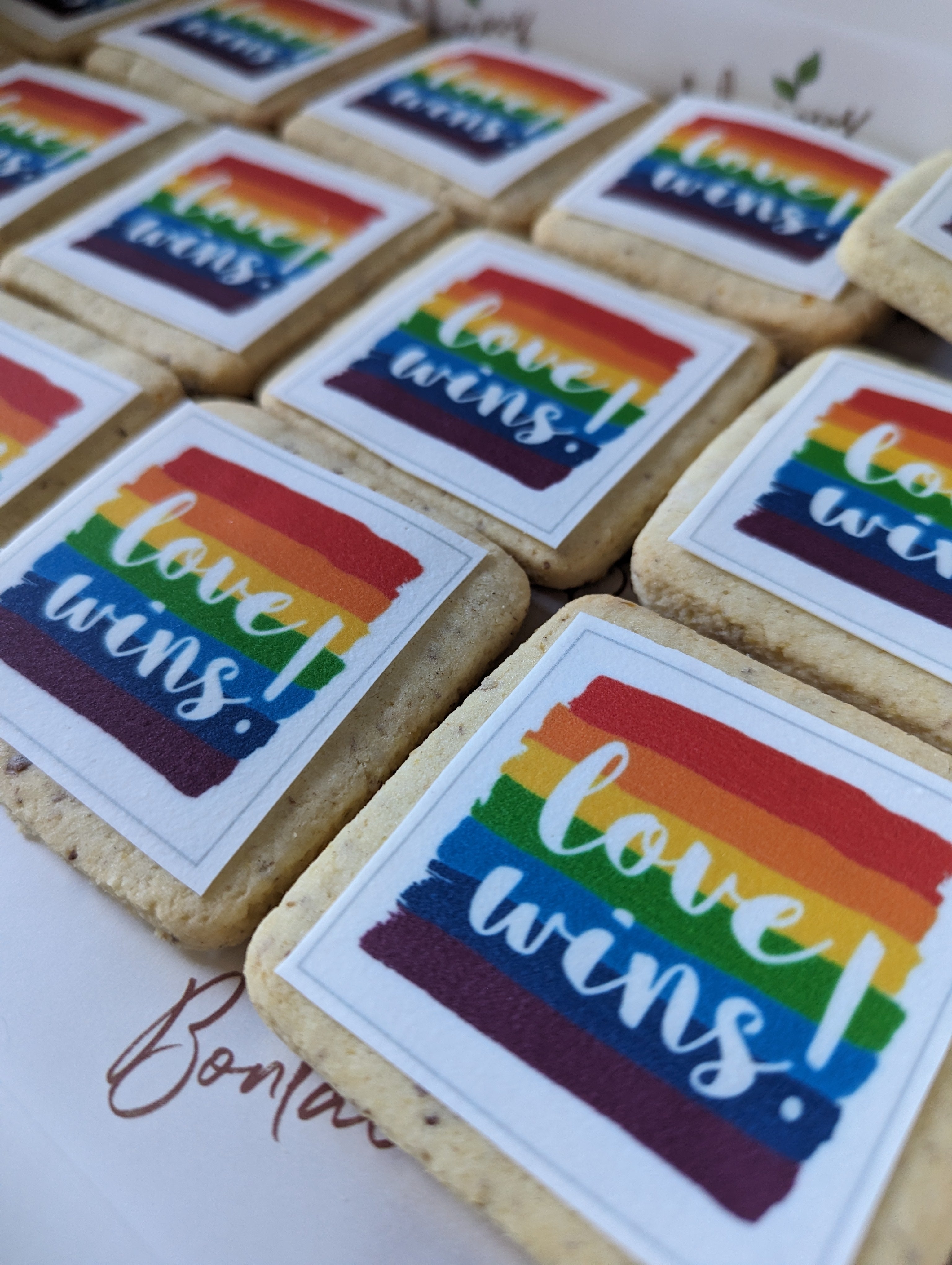 Cookies with rainbow-colored 'love wins!' stickers on a white surface.