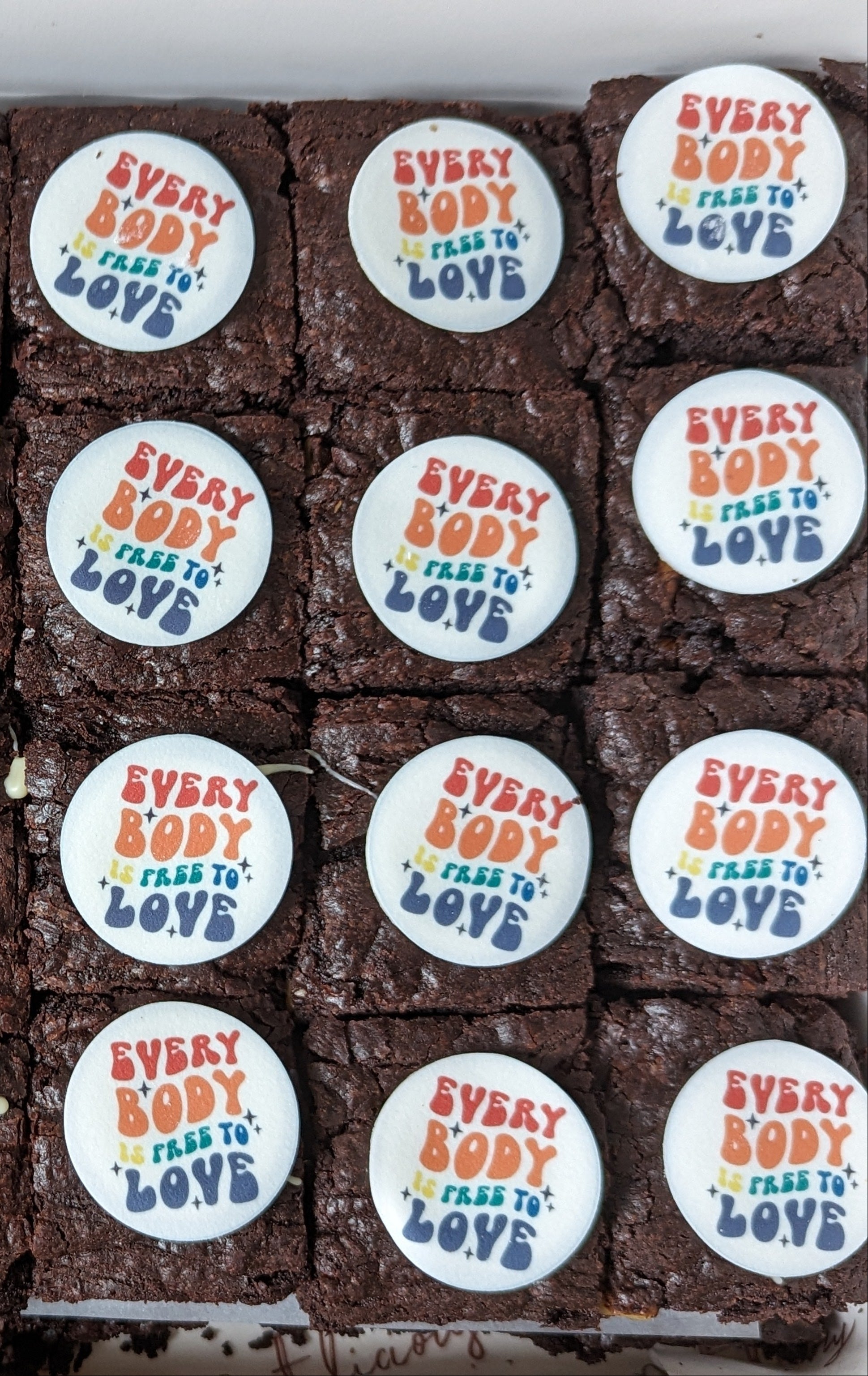 Brownies with decorative icing and 'Every Body is free to love' edible topper on a tray
