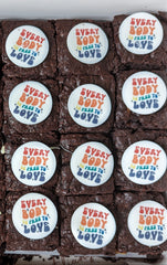 Brownies with decorative icing and 'Every Body is free to love' edible topper on a tray