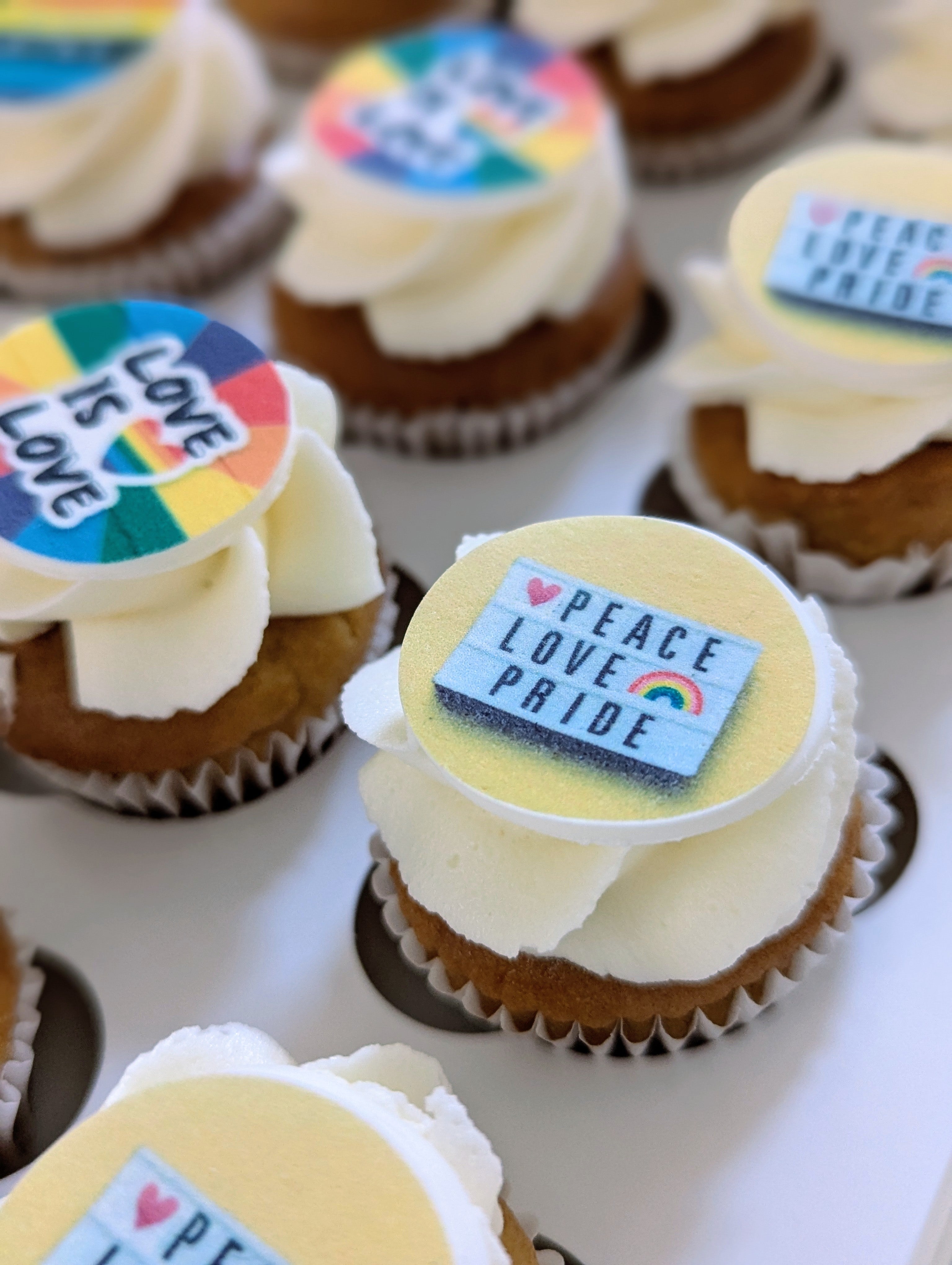 Cupcakes with 'Peace Love Pride' and rainbow-themed decorations on a white tray.